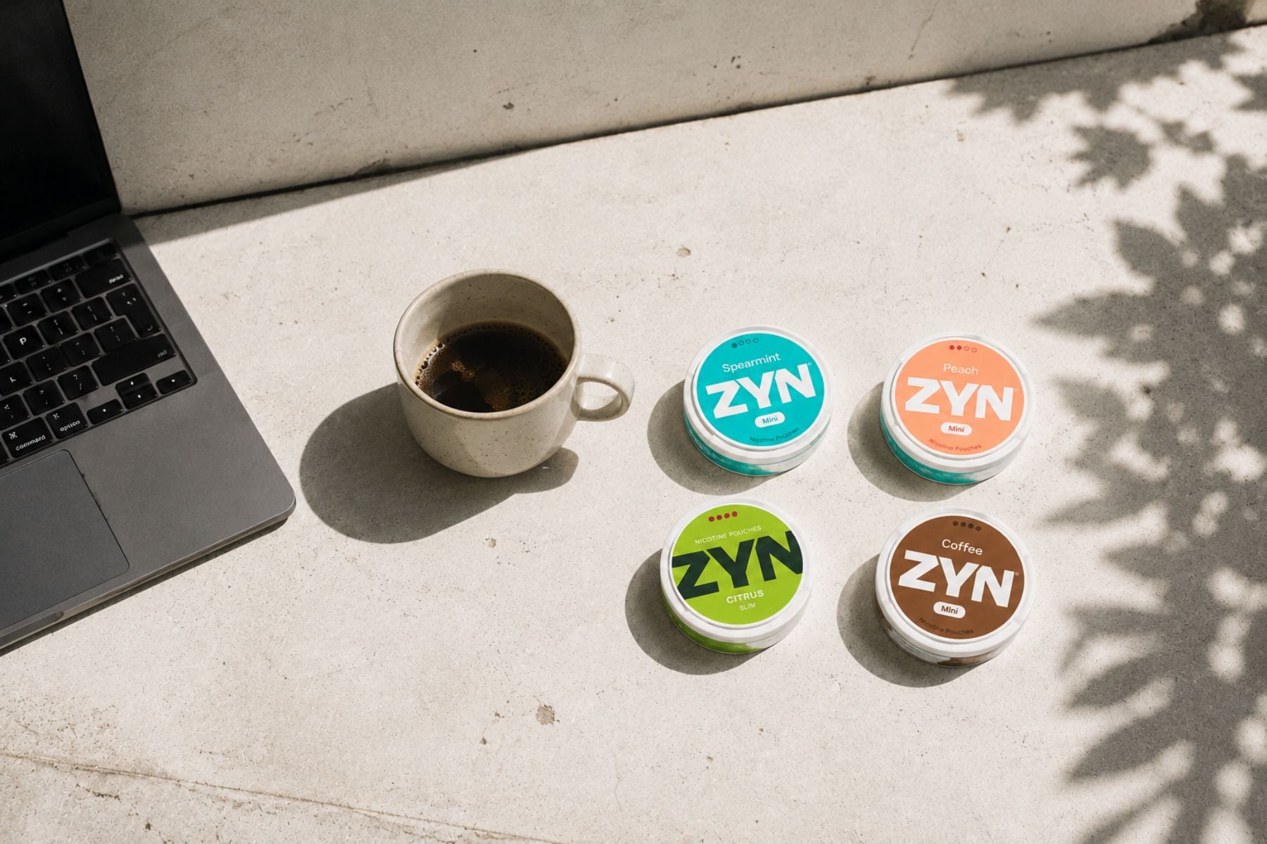ZYN nikotinpåsar på betong bredvid kaffekopp och laptop
