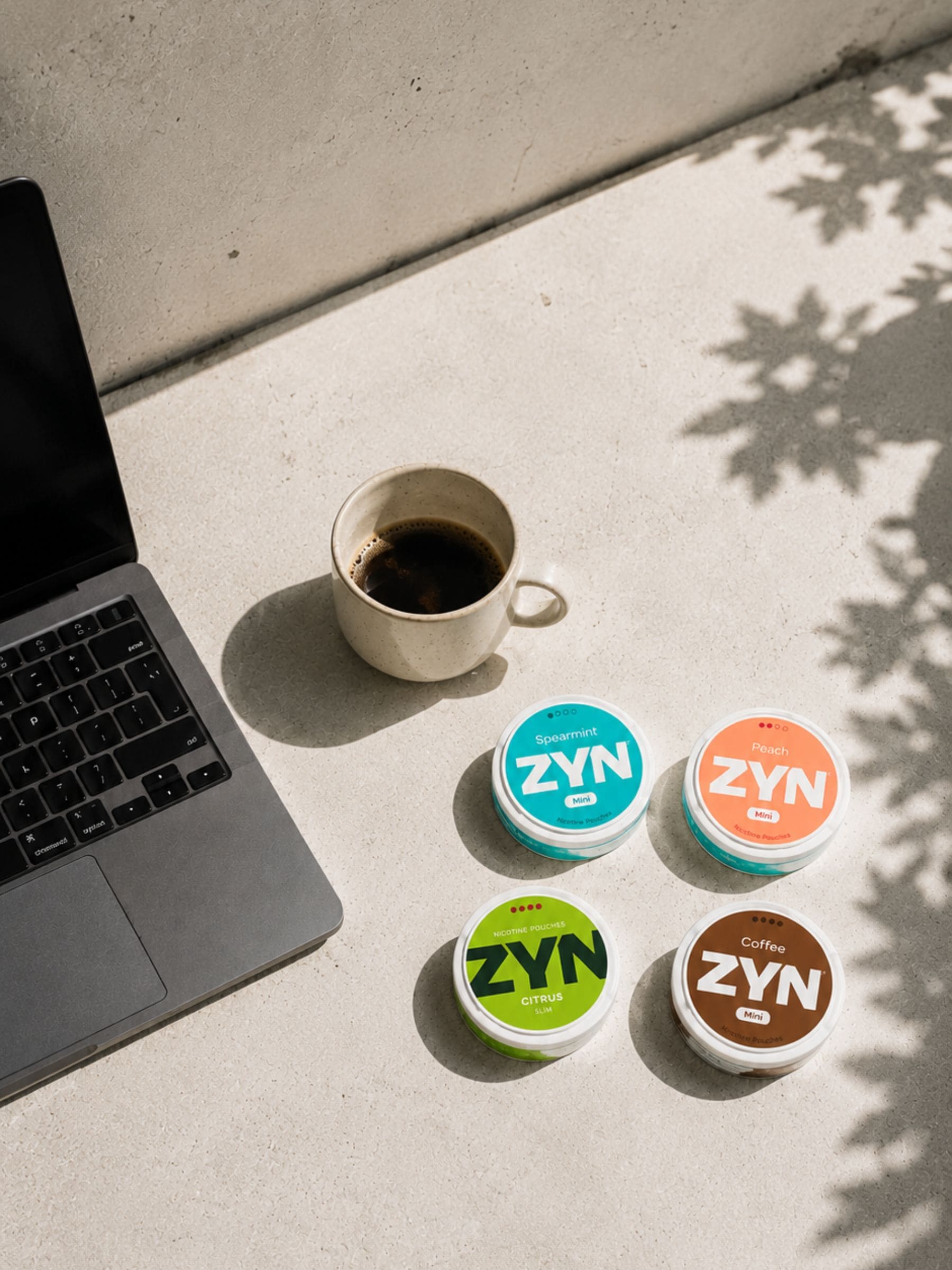 ZYN nikotinpåsar på betong bredvid kaffekopp och laptop